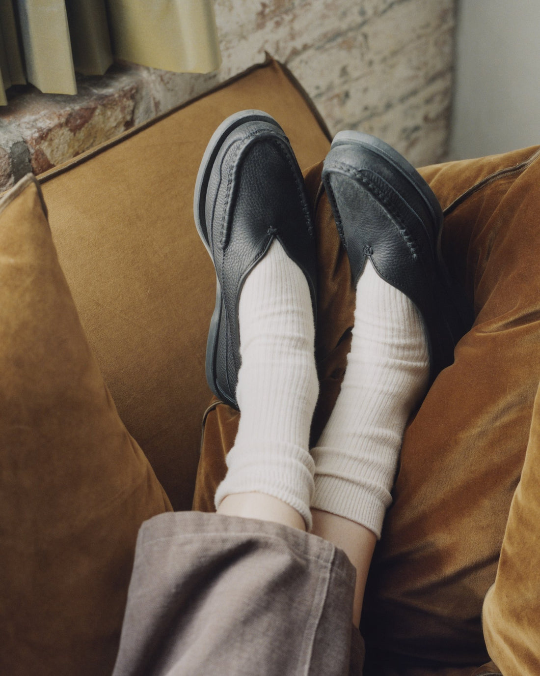 Feet up on a velvet sofa in black Sirah loafers and white socks