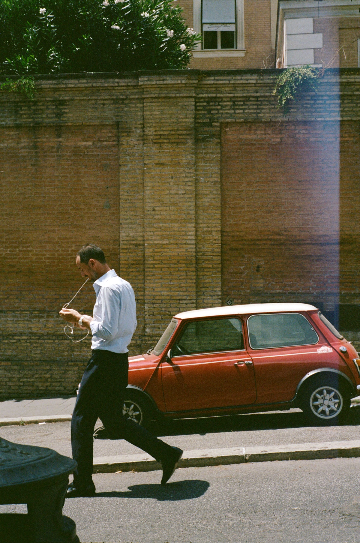 A man in a white shirt walking past a red Mini on a street in Rome