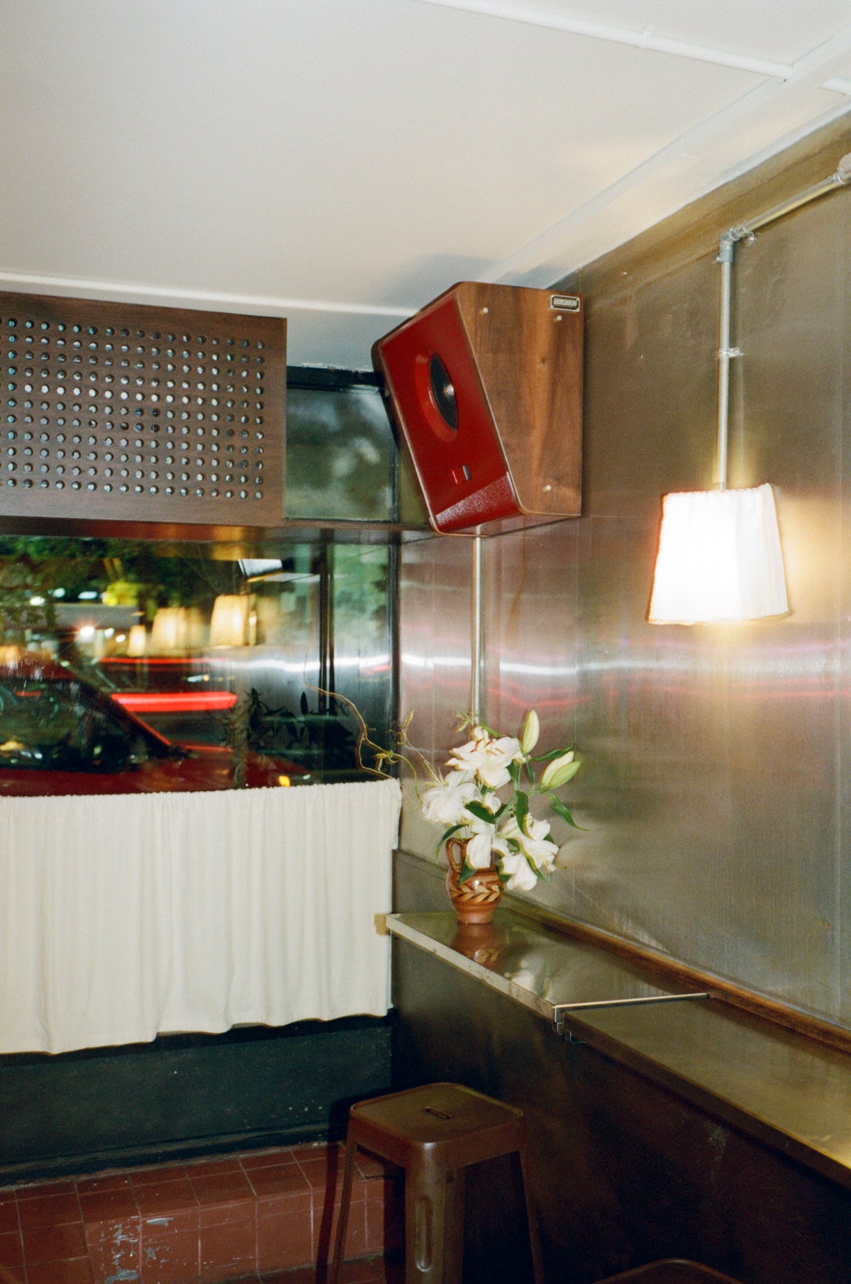 The steel bar at Colbo Next Door, a paper lamp lit above the counter
