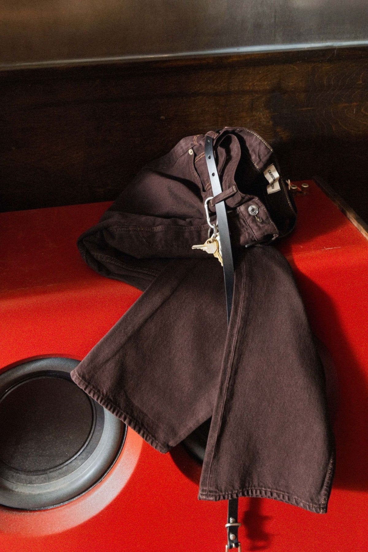 Carson Wach 333 Original Jeans in the Colbo exclusive brown wash with a black belt and keys, draped over a red speaker