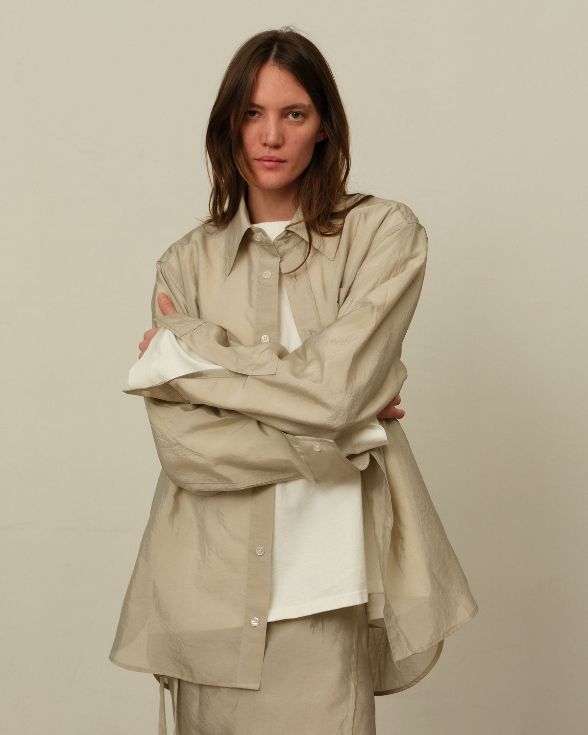 A model with arms crossed in a sheer greige shirt over a white long-sleeve tee