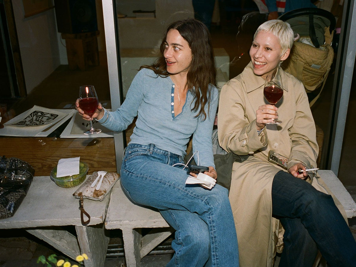 Two friends with red wine on the bench outside the shop