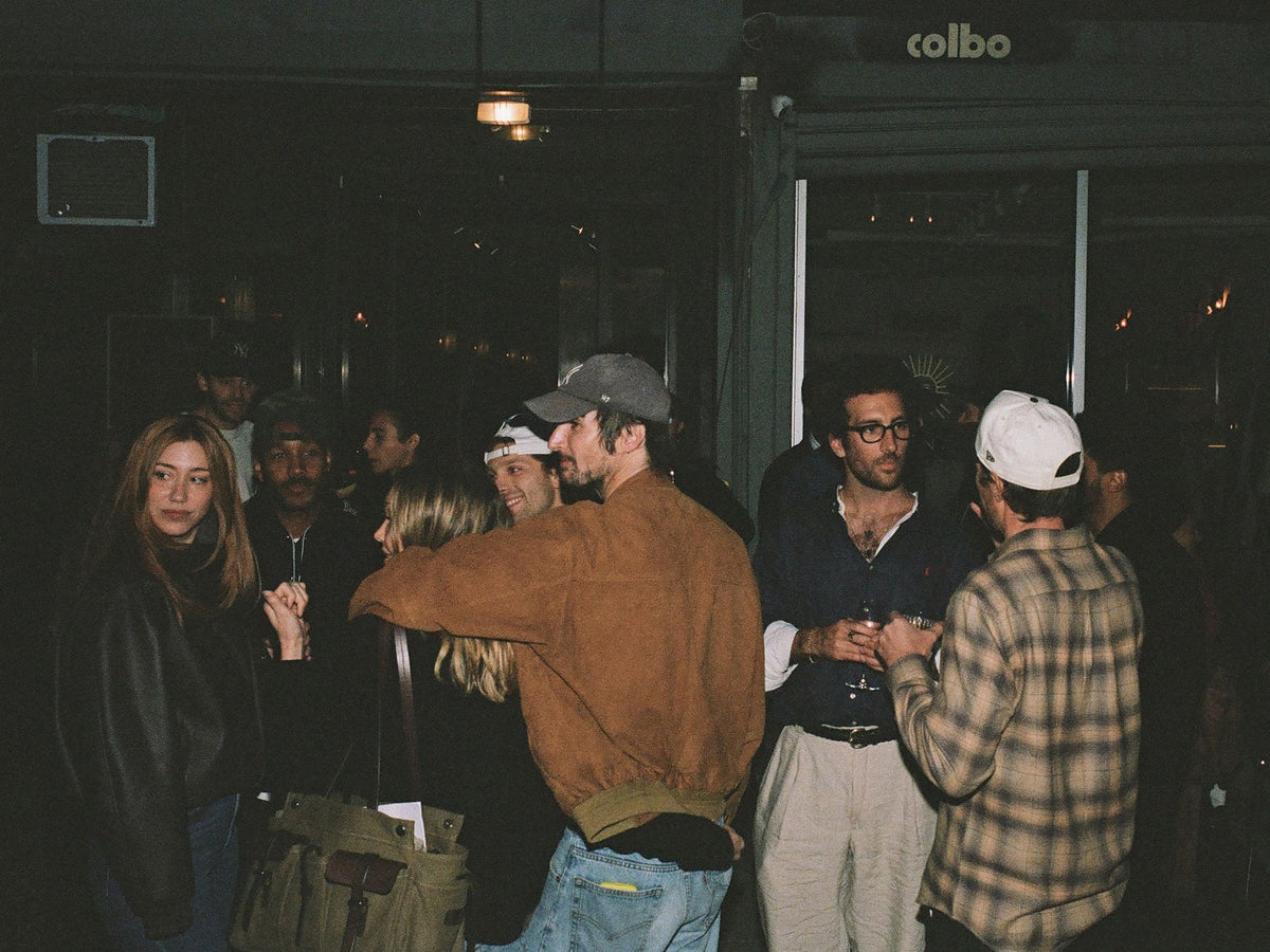 A crowd on the sidewalk under the Colbo sign at night