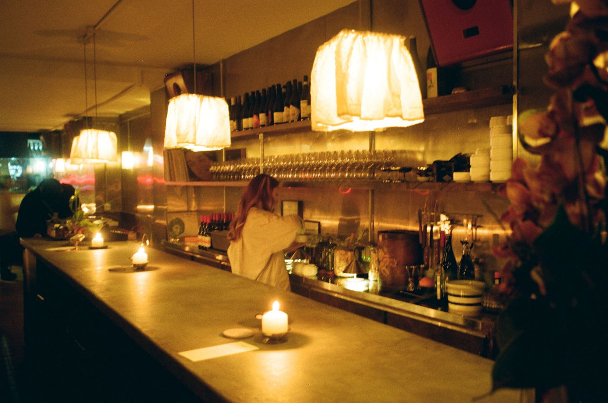 Candles along the bar at Next Door, wine bottles and glasses on the shelves behind