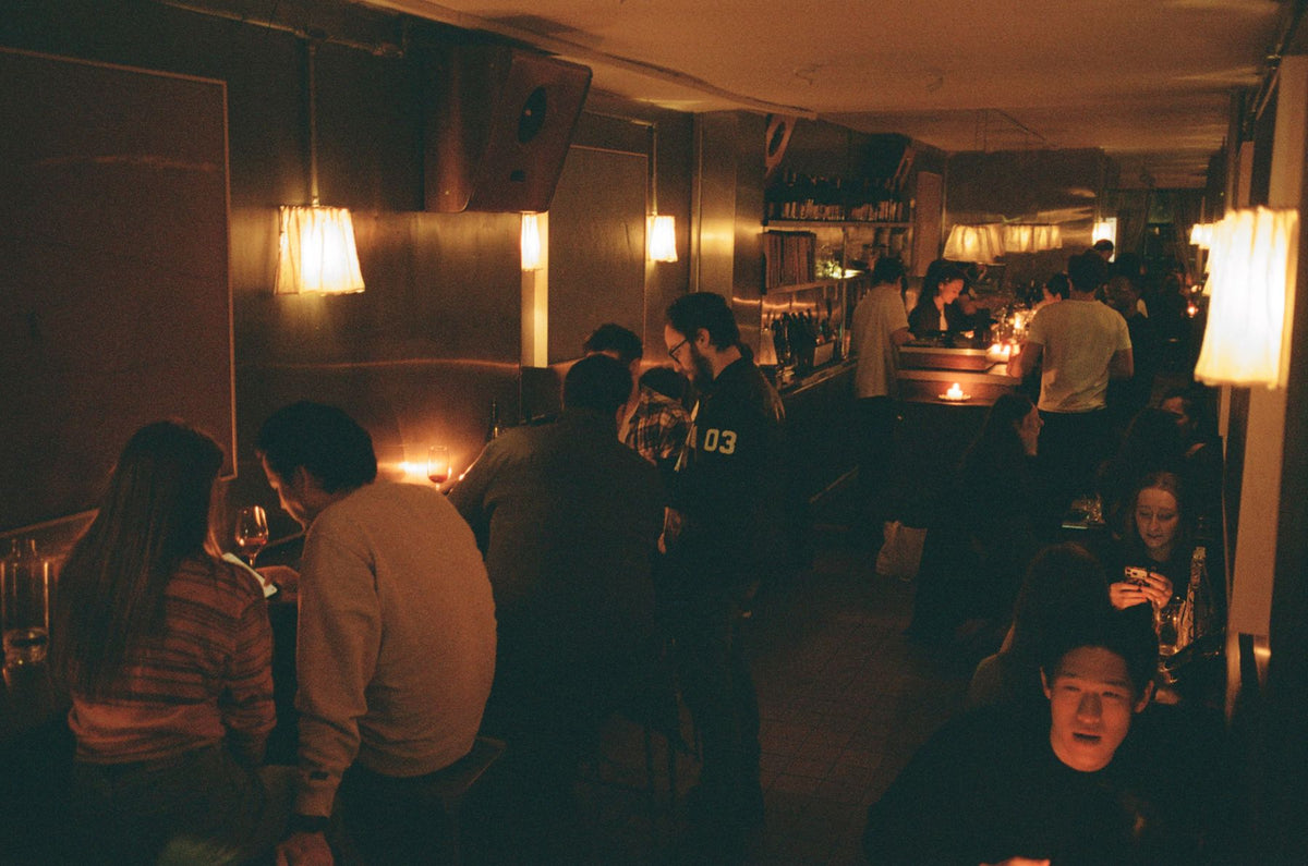 A full room at Next Door, people talking at the tables under the wall lamps