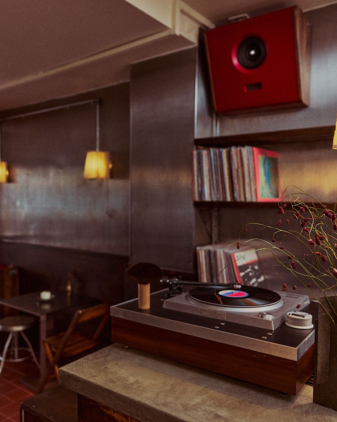 The turntable at Next Door, records on the shelf and a red speaker above
