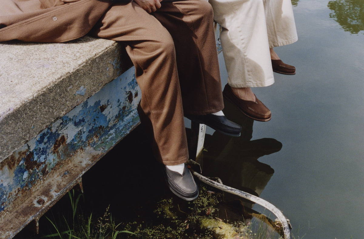 Feet over the water off a painted dock, in black and chocolate Sirah loafers