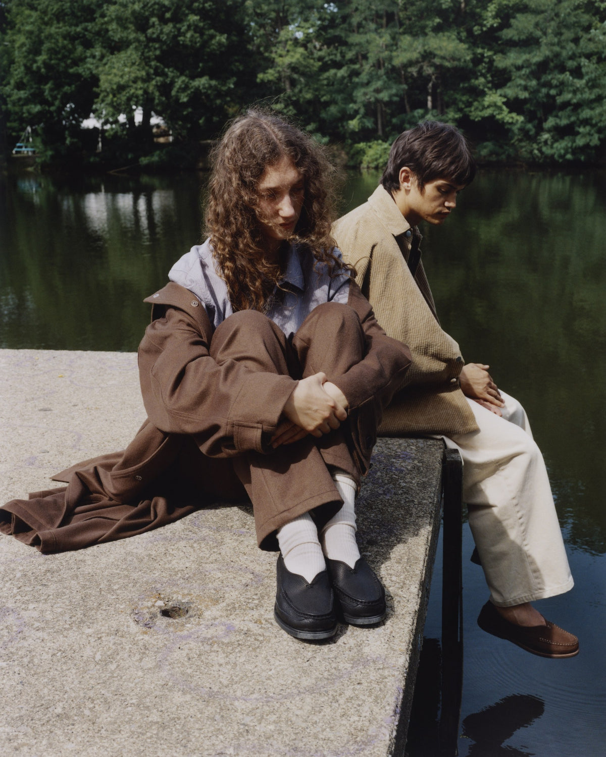 Two people sitting on the edge of a dock in black and chocolate Sirah loafers