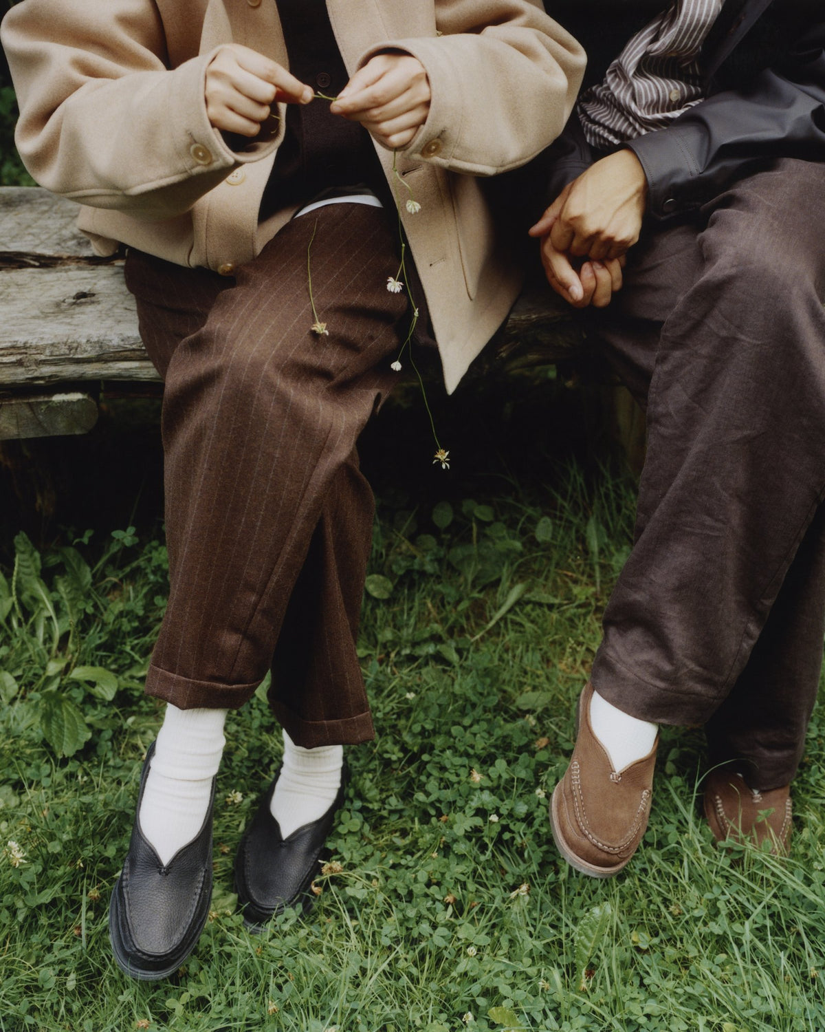 Two people on a bench in the grass, in black and chocolate Sirah loafers