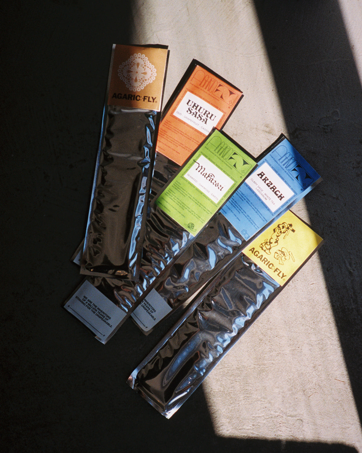 Agaric Fly Incense, five packets in colored sleeves on concrete in raking sunlight