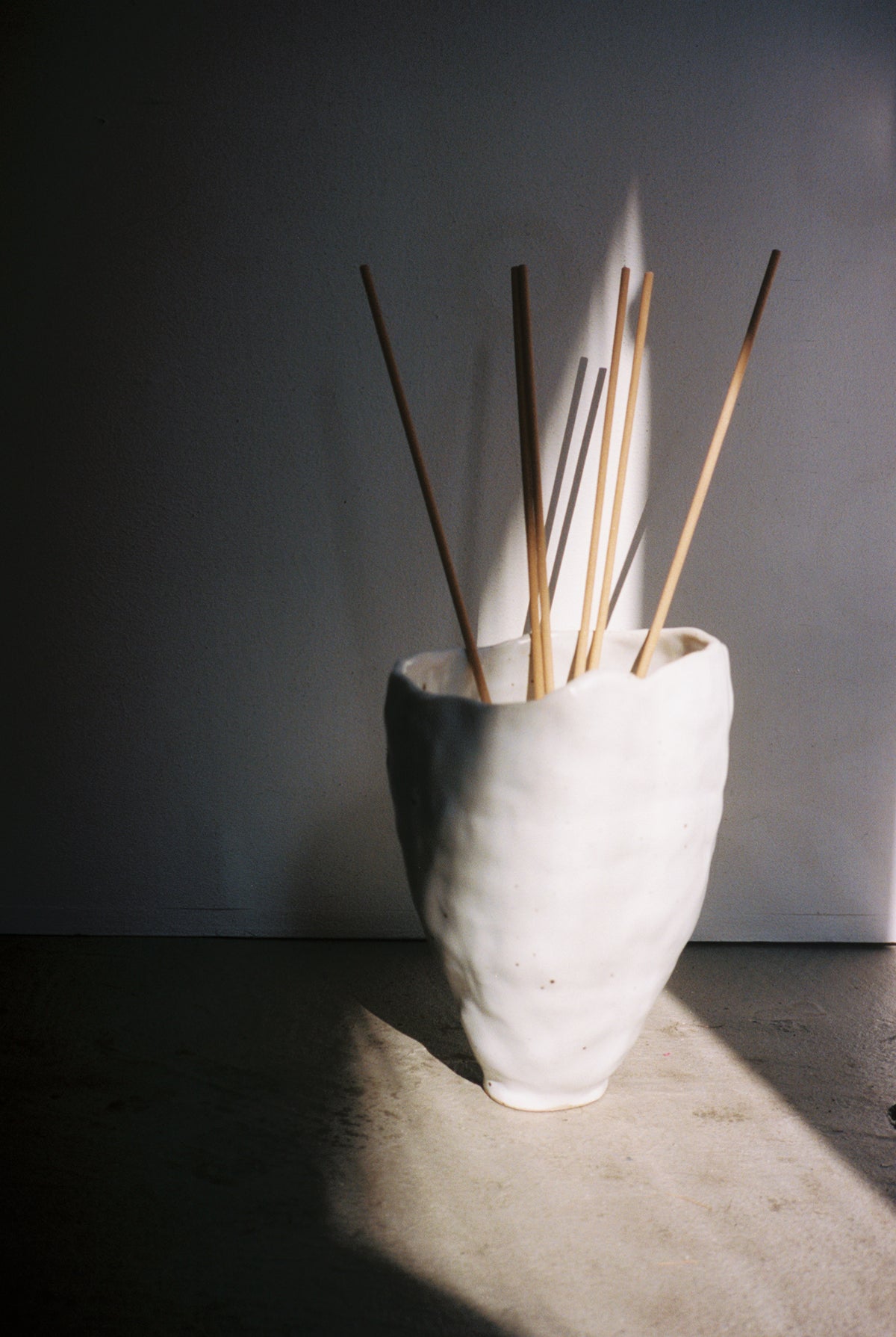 Agaric Fly Incense sticks standing in a white ceramic vase in raking light